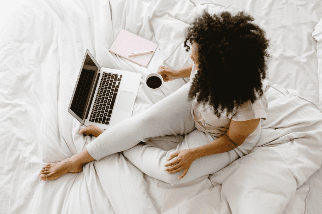 Woman searching up the benefits of increased productivity on her laptop while drinking coffee in bed.