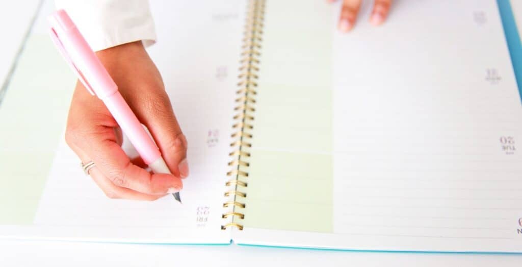 A hand is shown writing inside of a planner as the woman doesn't beleive the planning misconceptions. 